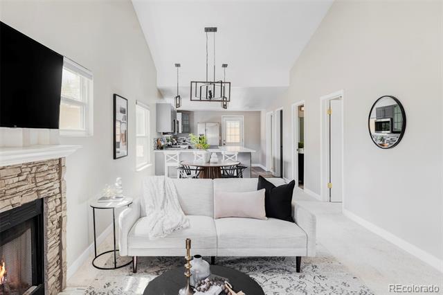 Staged living room with a white sofa, stone fireplace, and open dining area.