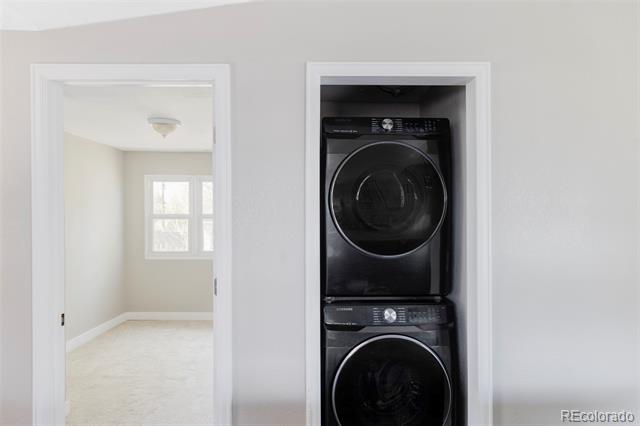 Stacked black washer and dryer in a closet beside an open doorway to a bright room.