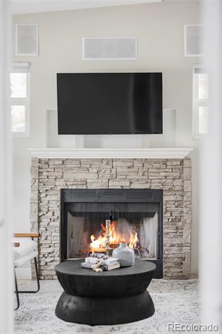 Living room with a lit stone fireplace, wall-mounted television, and round black coffee table.