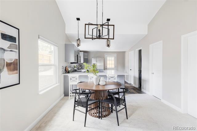 Dining area with a round wood table, black chairs, and a geometric pendant chandelier beside the kitchen.
