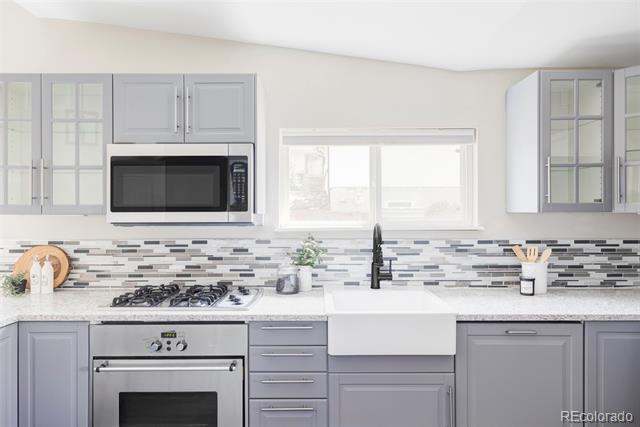 Kitchen with gray cabinets, stainless appliances, a farmhouse sink, and a patterned tile backsplash.