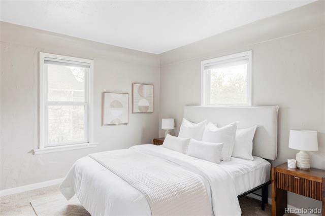 Bright bedroom with a white bed, upholstered headboard, and two windows.