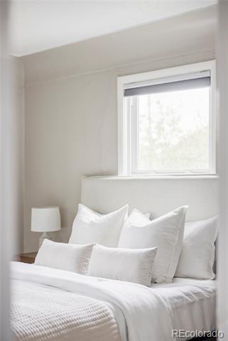 Bright bedroom with a white bed, layered pillows, and a window with a partially lowered shade.