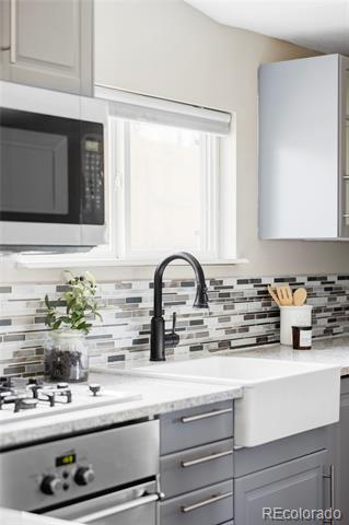 Kitchen with white cabinetry, stainless steel appliances, farmhouse sink, and gray mosaic backsplash.