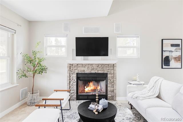 Living room with a stone fireplace, wall-mounted television, white seating, and black coffee table.
