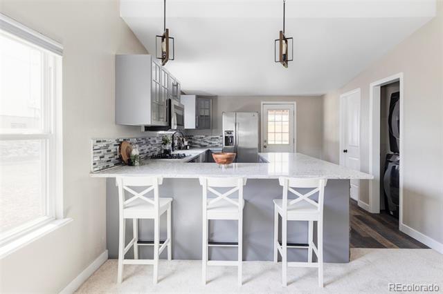 Kitchen with gray cabinets, stainless appliances, patterned backsplash, and a white island with three stools.