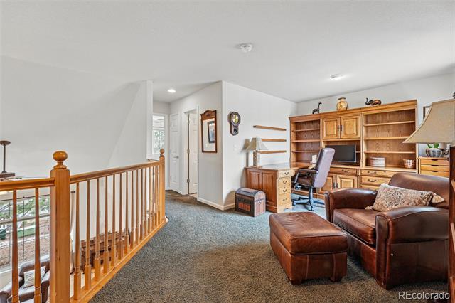 Furnished loft with built-in wooden bookcase, desk, brown leather seating, and a railing overlooking the stairs.