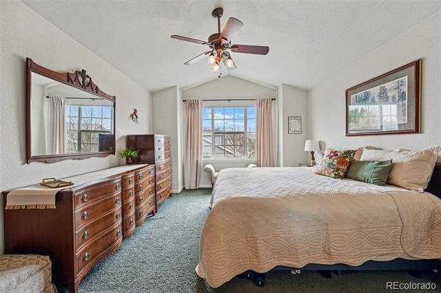 Furnished bedroom with a large bed, wooden dressers, and a window overlooking neighboring homes.