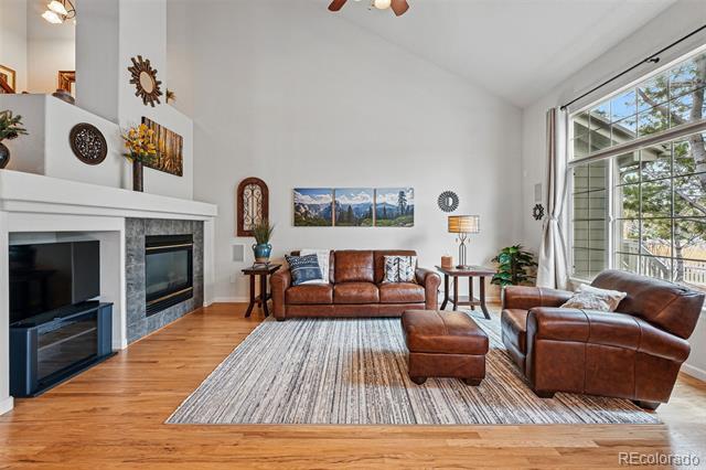 Living room with vaulted ceilings, a white fireplace, large windows, and brown leather seating.