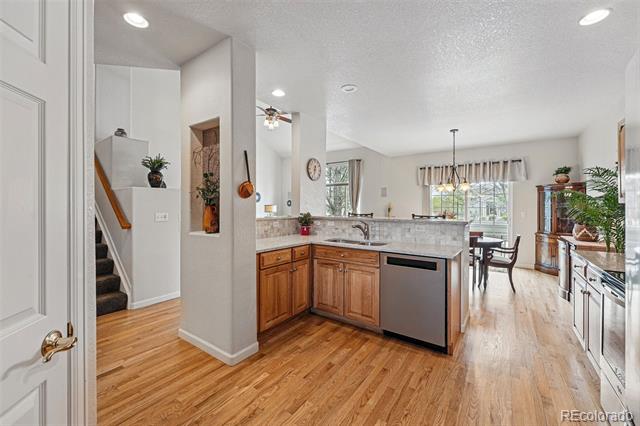 Open kitchen with wood cabinets and flooring, granite island, stainless-steel dishwasher, and adjoining dining area.