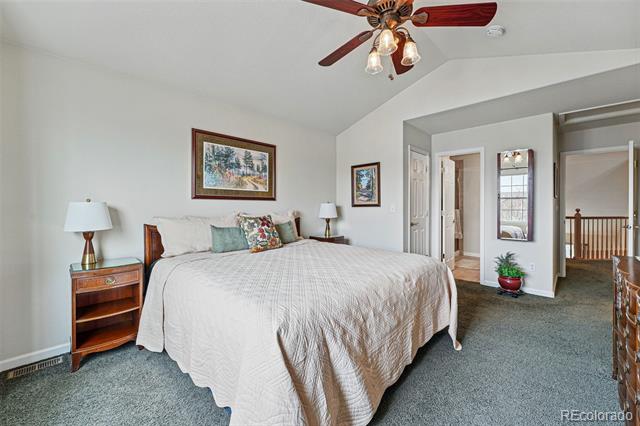 Furnished bedroom with a large bed, gray carpet, ceiling fan, and an open doorway to the hall.