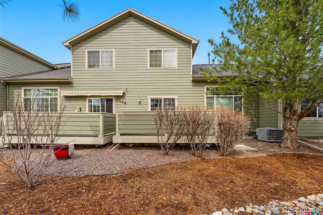 Rear exterior of a sage-green two-story house with a raised deck and dormant landscaping.