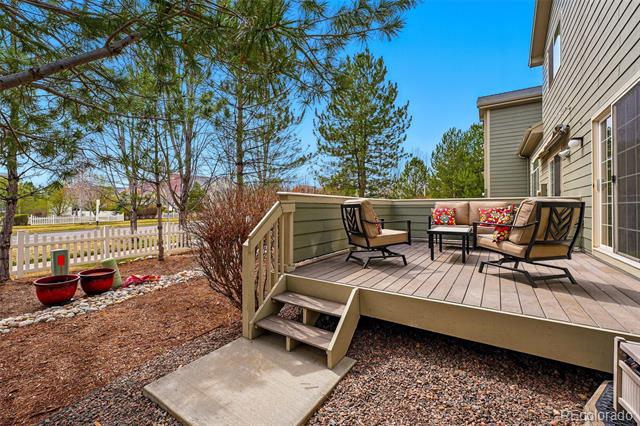 Raised deck with outdoor seating beside the house, overlooking a fenced yard and pine trees.