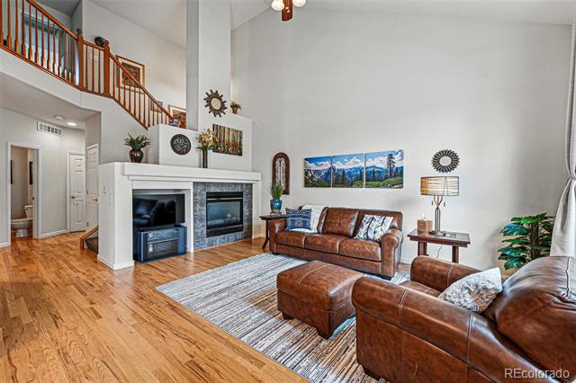 Living room with vaulted ceiling, white fireplace and built-in media niches, hardwood floors, and brown leather seating.