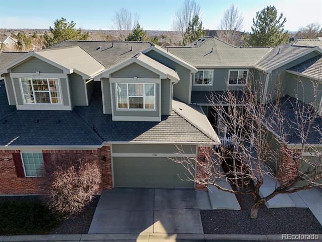 Gray two-story home with brick facade, front-facing garage, and leafless trees, seen from above.