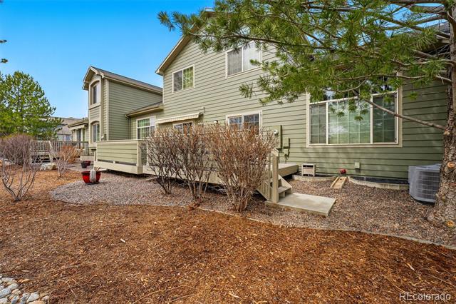 Rear exterior of a green two-story house with a raised deck and gravel landscaping.