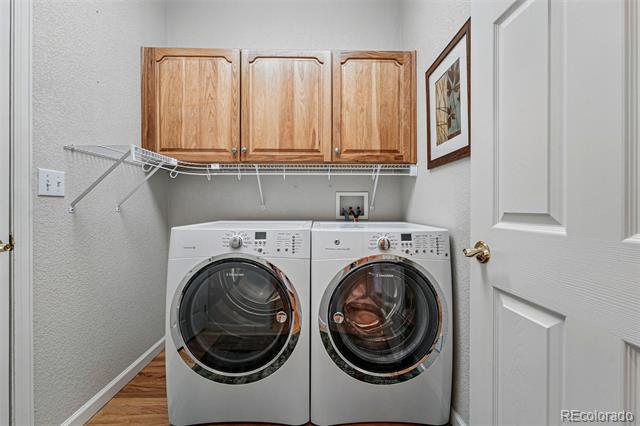 Laundry room with front-loading washer and dryer beneath wooden cabinets.