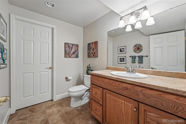 Bathroom with a wood vanity and oval sink, large mirror, toilet, and brown tile floor.