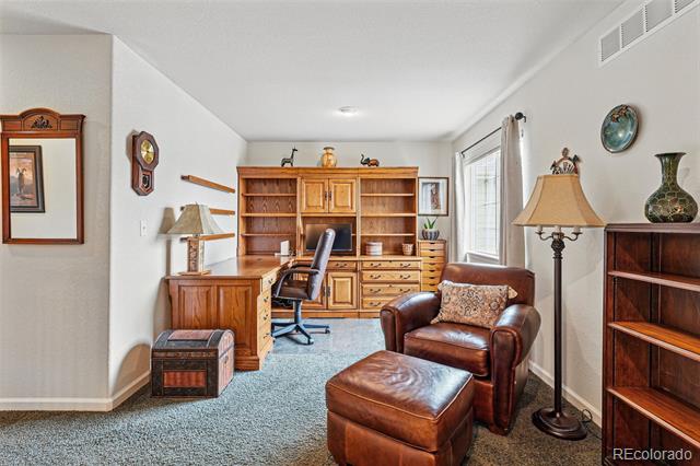 Home office with built-in wooden desk and bookcase, leather armchair, and ottoman.