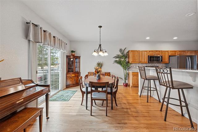 Dining area with round table and chandelier beside a wood-cabinet kitchen and breakfast bar.