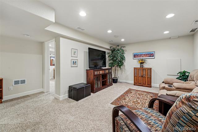 Basement recreation room with carpet, a television and entertainment center, and upholstered seating.
