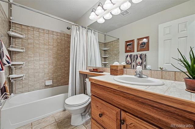 Bathroom with a tiled tub and shower, toilet, and wood vanity with a white countertop.