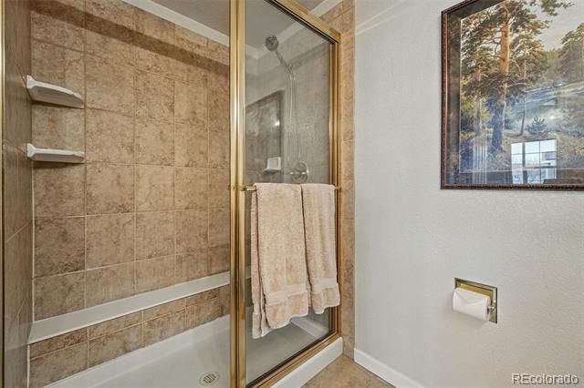 Bathroom tub with tan tile, gold-framed glass doors, built-in shelves, and a framed wall picture.