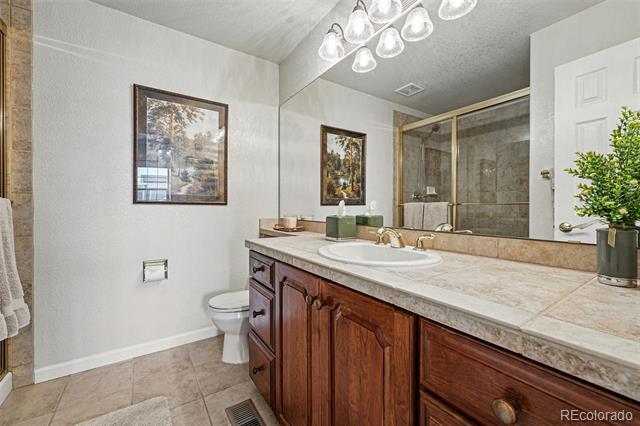 Bathroom with a dark wood vanity, stone countertop, and mirrored glass shower enclosure.