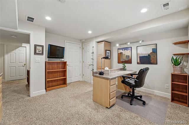 Home office with a wood desk, black chairs, beige carpet, and framed artwork.