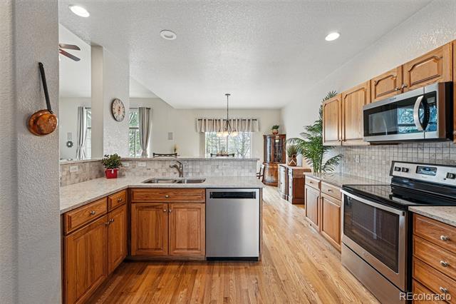 Kitchen with wood cabinets, granite counters, stainless steel appliances, and wood floors leading to a dining area.