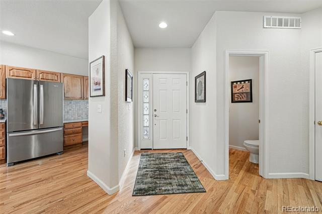 Entry hall with a glass-sidelight front door, wood floors, and a view into the kitchen and bathroom.