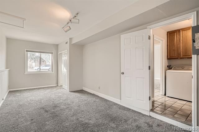 Empty carpeted room with a closet, window, and adjoining laundry area.