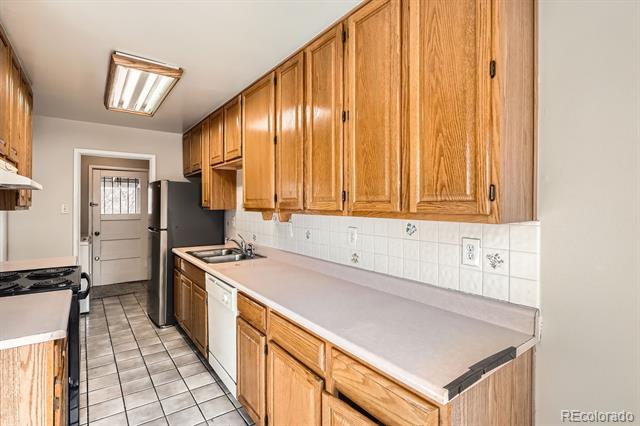 Galley kitchen with honey-colored wood cabinets, pale countertops, and tiled flooring.