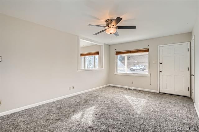 Empty carpeted room with two windows, a white entry door, and a ceiling fan.