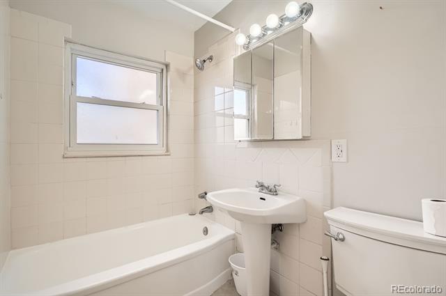 Bathroom with a white bathtub, pedestal sink, mirrored medicine cabinet, and window.