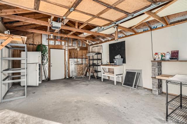 Garage with exposed wooden rafters, concrete floor, metal shelving, and a workbench.