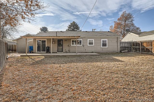 Rear of a ranch-style home with a fenced, leaf-covered backyard and concrete patio.