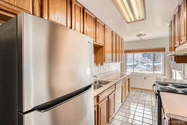 Kitchen with wood cabinets, stainless-steel refrigerator, and a large window overlooking parked cars.