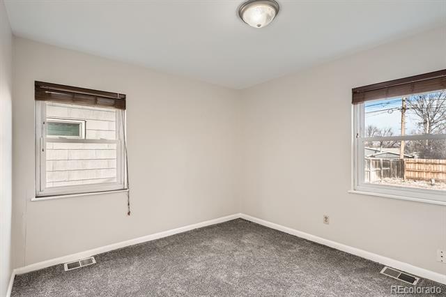 Empty carpeted room with two windows overlooking a fenced yard.