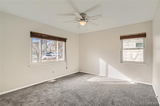 Vacant bedroom with gray carpet, two windows, and a ceiling fan.