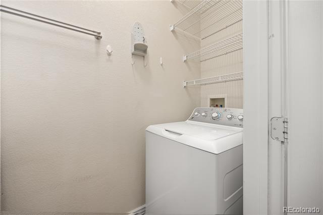 Laundry room with a top-loading washer and wire shelving.