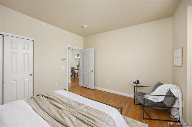Bedroom with a bed, a gray armchair draped in white, and an open doorway to the dining area.