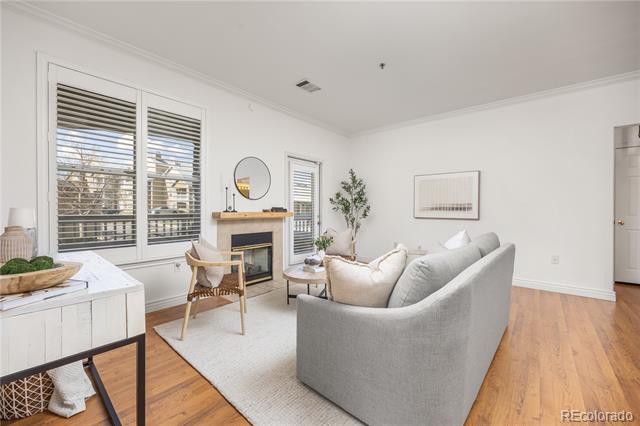 Living room with gray sofa, fireplace, plantation-shuttered windows, and light wood floors.