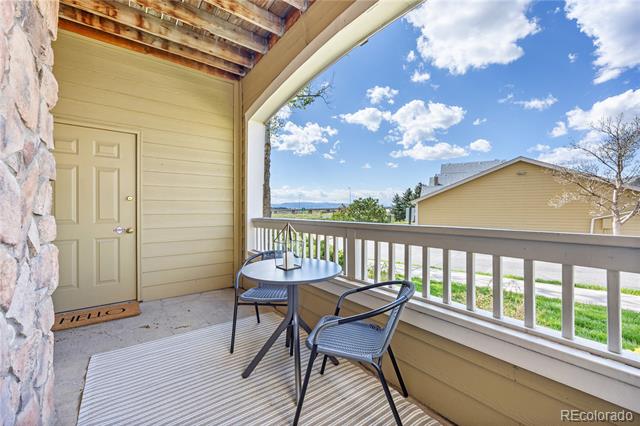 Covered balcony with two chairs and a table overlooking a neighboring building.