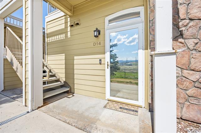 Condominium entrance D14 with a glass door, beige siding, and exterior stairs.