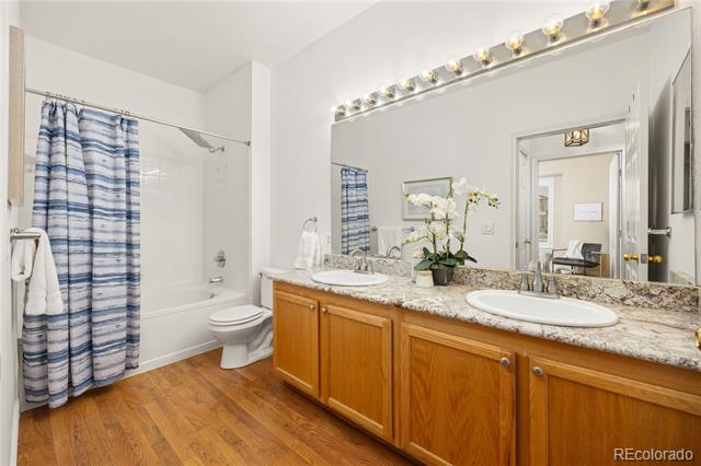 Bathroom with a double-sink wood vanity, large lit mirror, and blue striped shower curtain.