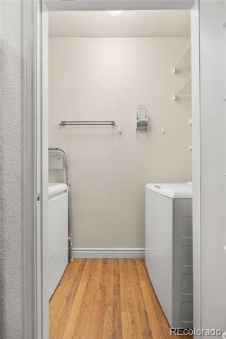 Laundry room with a washer and dryer, wall-mounted drying rack, and wood flooring.