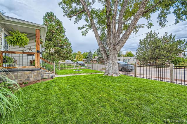 Fenced lawn and large shade tree beside the home’s covered porch.