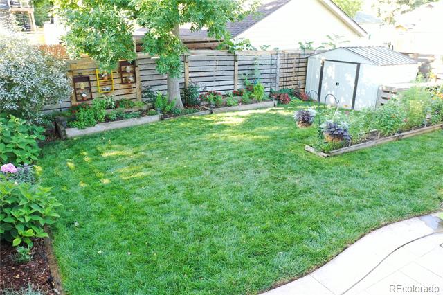 Backyard lawn bordered by garden beds, a wooden privacy fence, and a gray garden shed.