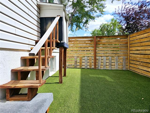 Fenced backyard with artificial turf and wooden stairs leading to an elevated deck.